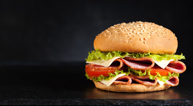 Sandwich burger with ham, cheese and vegetables on a black background and space for text