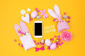 Smartphone mock up  with Easter decoration: eggs, bunny bag and candy on yellow background