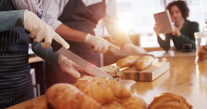 Waiter and waitress cutting bread loaf and sandwich at counter in cafe 4k