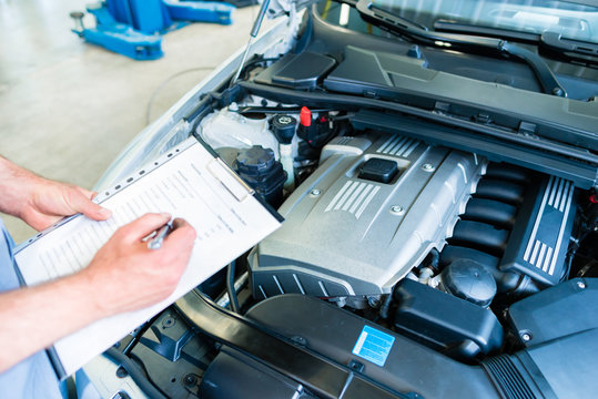 Mechaniker kontrolliert Auto mit Checkliste in Kfz-Werkstatt 