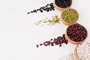 Assortment of haricot in a wooden bowls with copy space and tracks beans on white wood background. Top view, closeup. Healthy protein food.