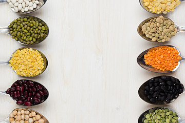 Assortment legume beans in spoons with copy space on white wood background. Top view, closeup.
