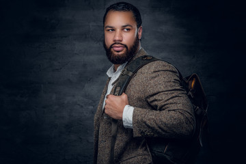Black man in a suit holds backpack.
