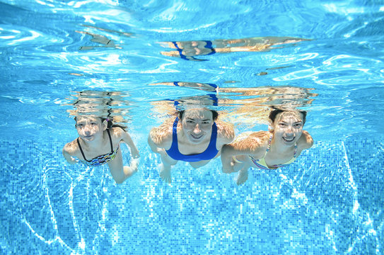 Family swims in pool under water, happy active mother and children have fun, fitness and sport with kids on summer vacation
