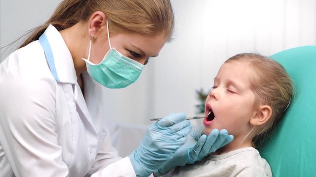 Milk teeth examination. Female dentist inspecting little patient mouth with mirror in clinic. 