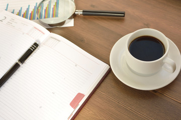 Financial documents, graphics, statistical calculations and a mug of coffee on a wooden background. Coffee time.