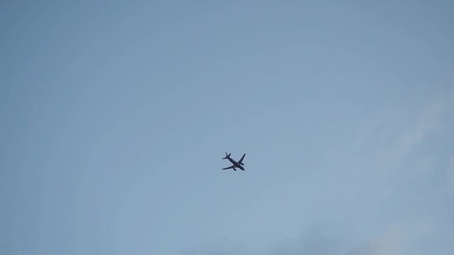 The small silhouette plane flying across the blue sky and clouds in slowmotion. 1920x1080