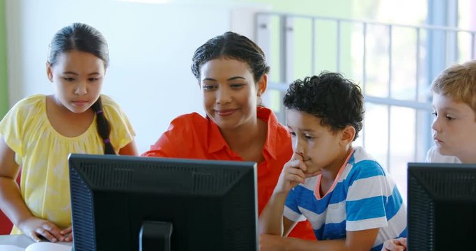 Teacher assisting schoolgirls in learning computer at school 4k