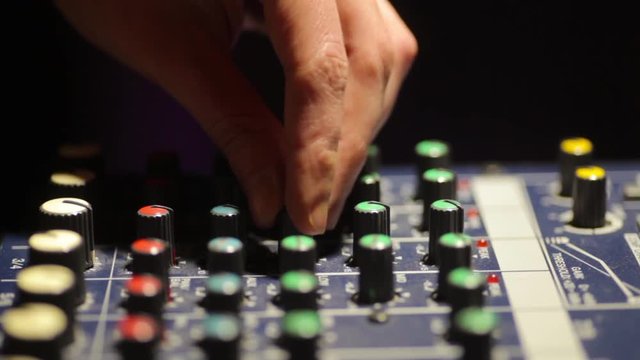 Close up video of a mixer desk with many buttons and and a hand adjusting levels.