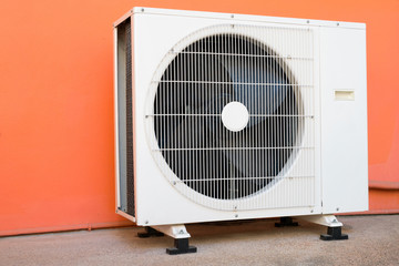 Condensing unit of air conditioner at a red-orange painted wall