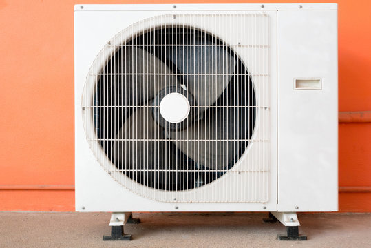 Condensing unit of air conditioner at a red-orange painted wall