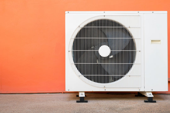 Condensing unit of air conditioner at a red-orange painted wall