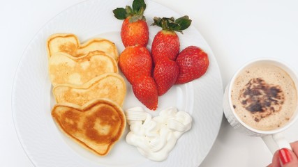 Heart-shaped pancakes with strawberry on a white dish.