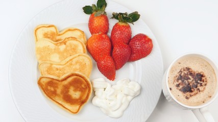 Heart-shaped pancakes with strawberry on a white dish.