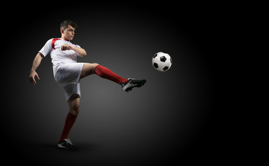 Football player is kicking a ball on the black background.