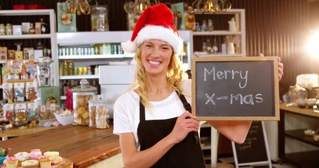 Portrait of smiling waitress showing chalkboard with merry x-mas sign in café 4k - Powered by Adobe