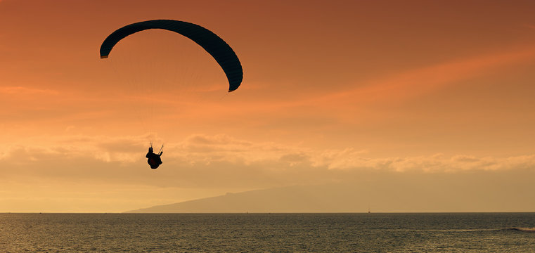 Paraglider flying at sunset over the ocean
