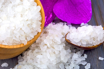 White bath salt in a wooden bowl with a spoon and an orchid