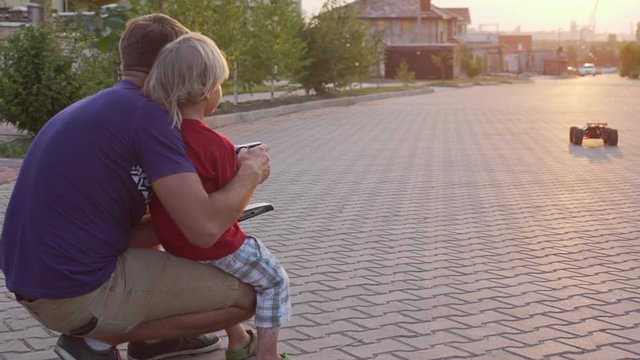 Young kid playing and his father playing with radio controlled car outside while sun setting down in slowmotion