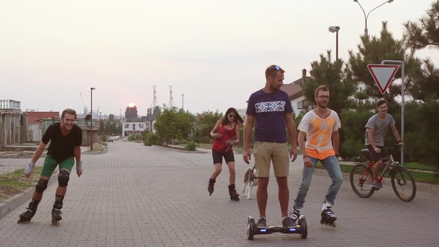 Five friends with husky dog rollerblading riding bicycle and gyroscooter outside having fun in slowmotion