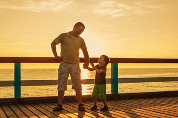 Dad and son playing at the pier on the sea at sunset
