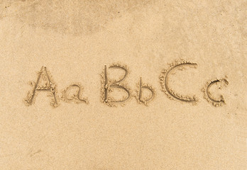 alphabet letters handwritten in sand on beach