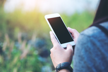 Mockup image of a woman using smart phone with blank black screen at outdoor and lake nature background