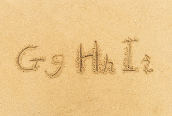 alphabet letters handwritten in sand on beach