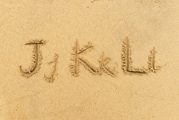 alphabet letters handwritten in sand on beach