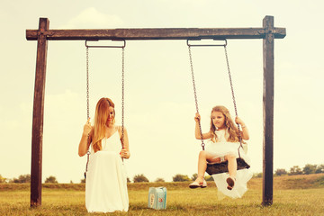 Mother and her daughter enjoy summer sunset on swing