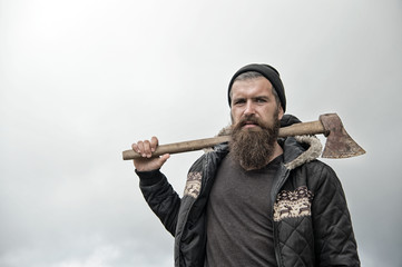 bearded handsome serious man with rusty axe against cloudy sky