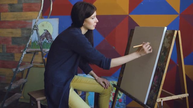 Young woman artist draw scetch wit pencil on easel canvas, preparing to paint picture