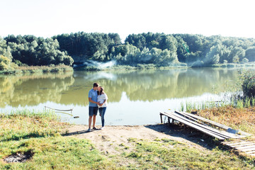 Charming expecting couple stands hugging by the green river