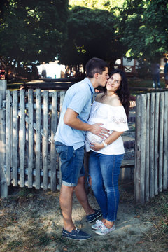Man kisses pregant woman while they stand by the wooden fence