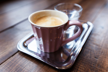 A pink cup of black coffee and a glass of water on a silver tray. Selective focus, small depth of field.