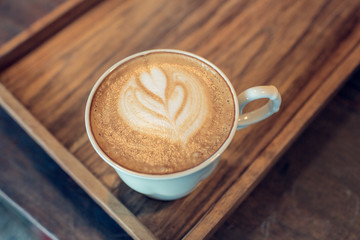 A cup of coffee with heart shape on wooden table,retro colors.