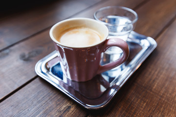 A pink cup of black coffee and a glass of water on a silver tray. Selective focus, small depth of field.