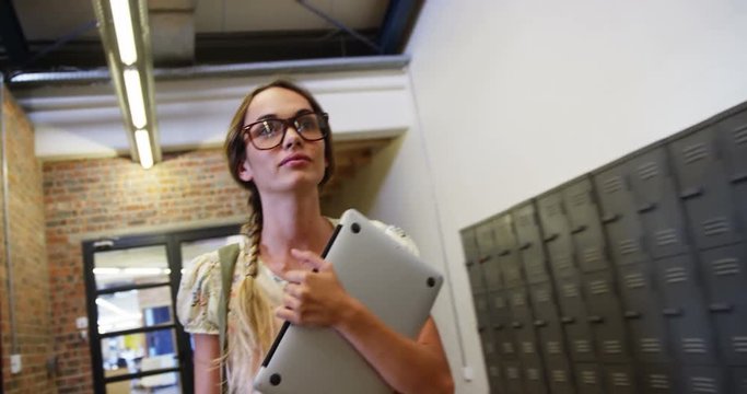 Portrait of business executive holding a laptop and walking on corridor in office 4k