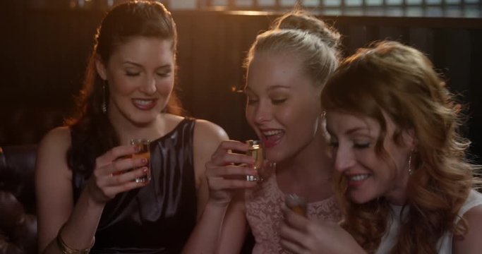 Three female friends toasting shot glasses of tequila in bar 4k