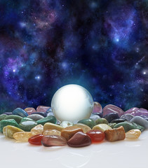 Crystal ball, healing crystals and the Universe - large clear crystal ball with a selection of chakra colored healing crystals with a background of the night sky deep space 
