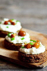 Canape with soft cheese and mushrooms on a board on a wooden background. Canapés cooked from rye bread, soft cheese and canned mushrooms. Simple appetizer recipe. Vertical photo. Closeup