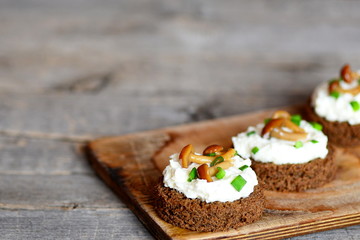 Vegetarian canape with soft cheese and mushrooms on a board on a wooden table. Canape cooked from brown bread, soft cheese and conserved mushrooms. Simple holiday appetizer. Closeup