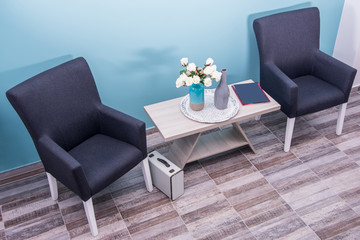 Overhead view of modern travel agency waiting room. Chairs, table, vase with flowers and suitcase.