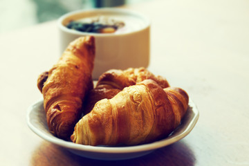Tasty fresh breakfast with croissants on plate on wooden table.