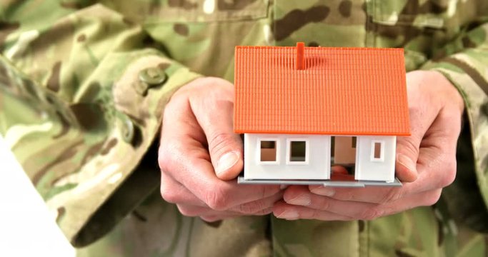 Mid section of soldier in military uniform holding house model on white background 4k