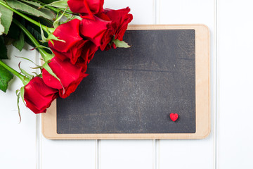 Bouquet of red roses and chalkboard on white wooden board. Space for text.