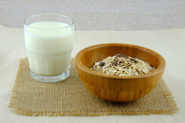 Glass of milk and wooden bowl with oat flakes on a burlap cloth.