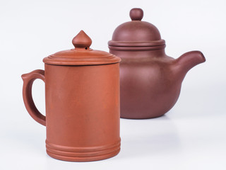 Picture of the brown infuser teapot near light brown tea cup. Infuser teapot and tea cup on white background. Handmade earthenware. Side view.