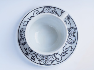 Close up coffee cup decorated with designs standing on a saucer isolated on white background. Top view.