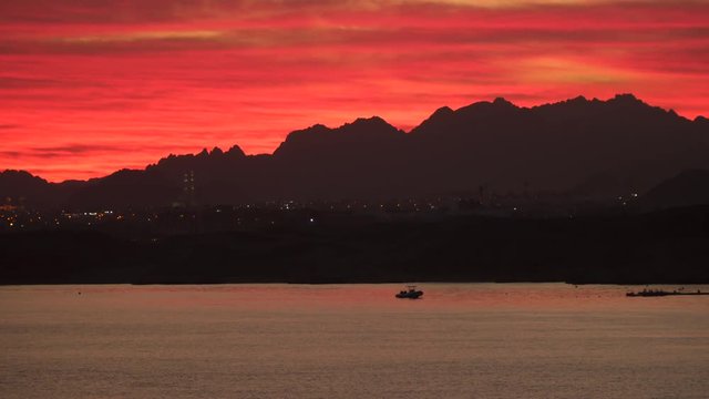 The lights of the city by the sea in the evening. One can see the outlines of the mountains. At sea, the boat